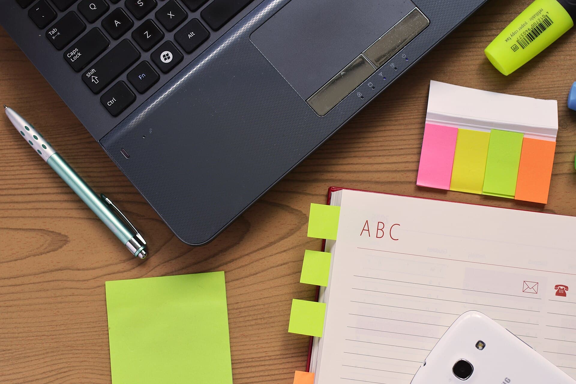 A laptop, notebook and pen on a timber desk